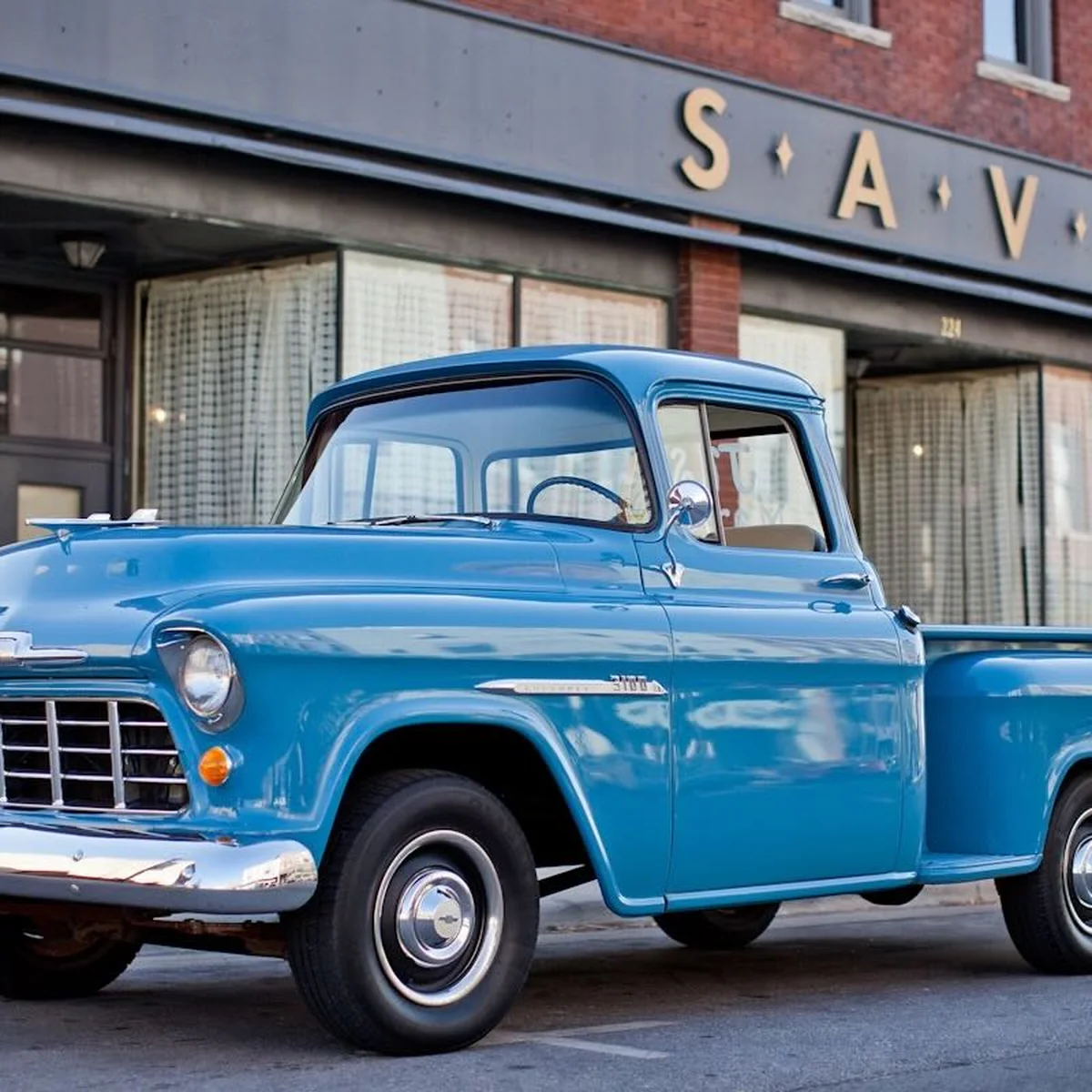A classic blue pickup truck in front of a brick storefront